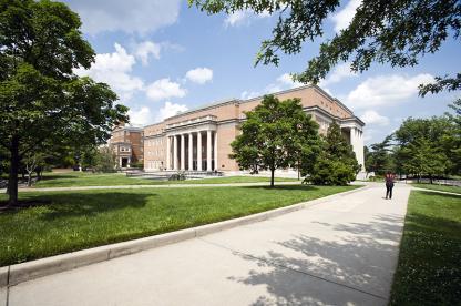 Large brick university library building with white columns, viewed from a concrete walkway.