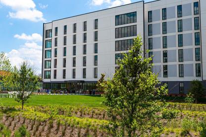 Modern multi-story white and grey residence hall building behind a green lawn with young trees.