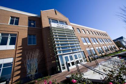 Front exterior of a multi-story brick campus building with a glass-enclosed main entrance.