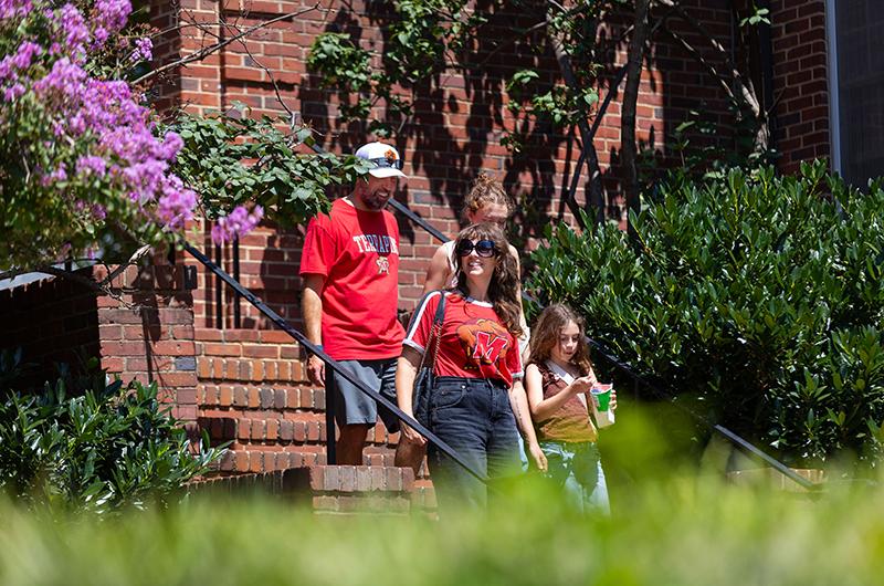 A family of four walks down a brick stairway framed by pink and purple flowers in the South Hill Community.