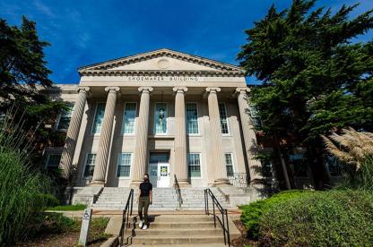 A woman walks down the steps of the Shoemaker Building, a stone structure with large columns.