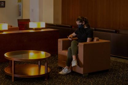 A student wearing a mask sits in a leather armchair in a dimly lit waiting area in the Counseling Center.